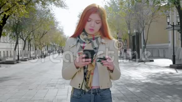 一个年轻的女孩站在一条城市街道上持有智能手机和银行卡通过信用卡进行电子支付视频的预览图