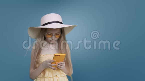 长头发的沙滩女孩正在蓝色背景上浏览手机视频的预览图