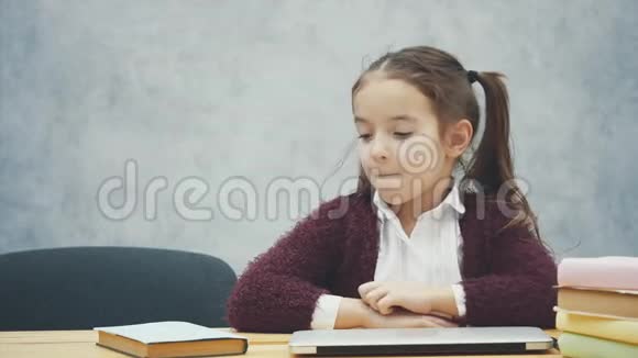 一个女学生坐在桌子旁在此期间选择一本书或笔记本电脑在灰色背景下快乐视频的预览图