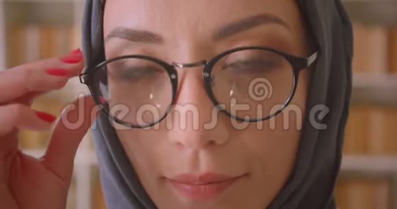 在图书馆里戴着眼镜戴着头巾的阿拉伯年轻女性脸上洋溢着笑容的特写镜头视频的预览图
