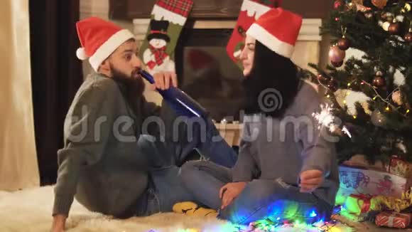 男人和女人坐在圣诞树附近女人手里拿着火花闪烁在前景模糊快乐视频的预览图