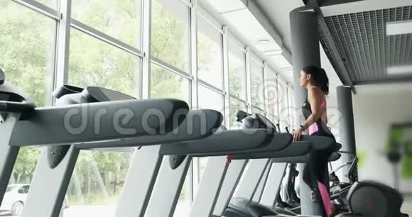 在体育俱乐部训练跑步模拟器的漂亮女人运动员女性在健身机上做运动行走视频的预览图