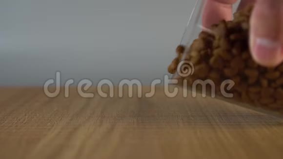 一个男人手从杯子里把脆脆的干猫粮洒在木头表面视频的预览图