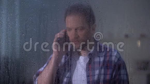 震惊的男人在雨窗后面打电话可怕的消息相对死亡视频的预览图