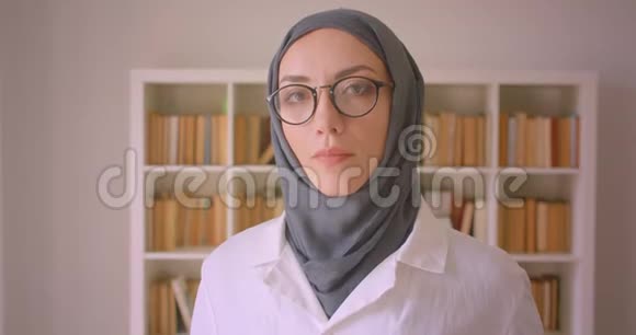 年轻的穆斯林女医生戴着眼镜戴着头巾在图书馆里兴高采烈地看着镜头的特写照片视频的预览图