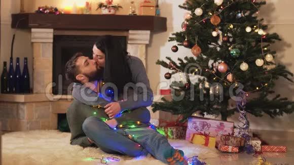 年轻的积极夫妇坐在房间地板上的圣诞树上新年和圣诞节的时间概念快乐视频的预览图