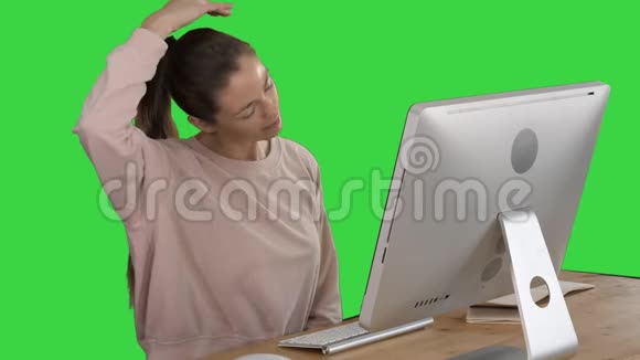 精疲力竭的年轻女性坐在家里的办公桌上按摩脖子上的绿色屏幕色度键视频的预览图