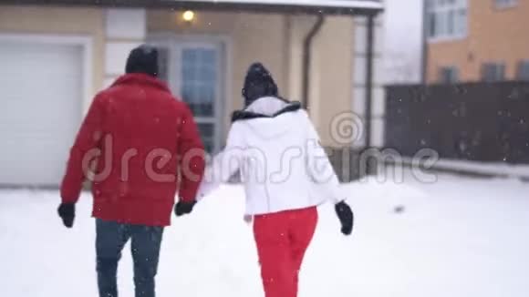 年轻的女人和留胡子的男人走在后院走向房子牵着手快乐的一对在冬天玩得开心视频的预览图