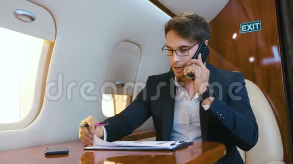 忙碌的商人在私人喷气式飞机上飞行时处理文件和在手机上交谈飞机视频的预览图