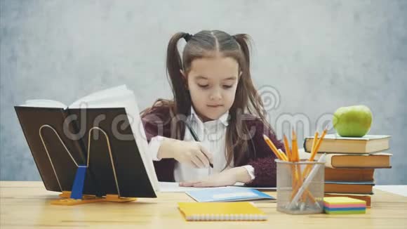 灰色背景的聪明女学生在这段时间里他坐在桌子旁写作业视频的预览图