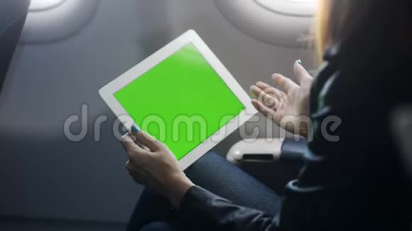 年轻女子坐在飞机上通过平板电脑在线会议与朋友或商业伙伴交谈视频的预览图