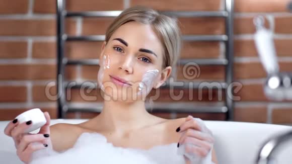 一幅美丽的女人的肖像在洗澡时看着相机脸上戴着奶油面具视频的预览图