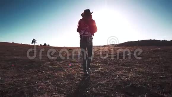 戴着帽子背着背包在夕阳下的田野上行走的苗条女运动员剪影视频的预览图