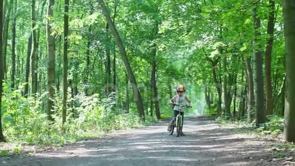 男孩骑自行车在城市公园的森林道路上视频的预览图