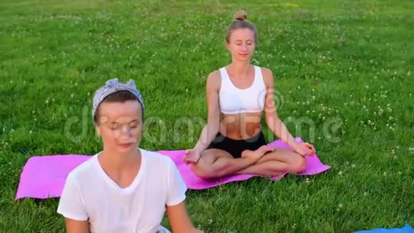 人们在公园的草地上练习瑜伽女孩们在冥想在日落时分坐在莲花的户外视频的预览图
