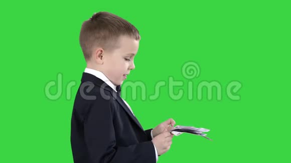 穿黑色西装的小男孩在绿色屏幕上数数钱Chroma键视频的预览图