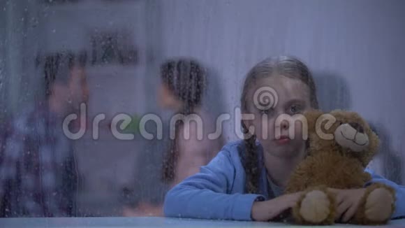 害怕的女孩在雨天拥抱泰迪熊听父母争吵视频的预览图