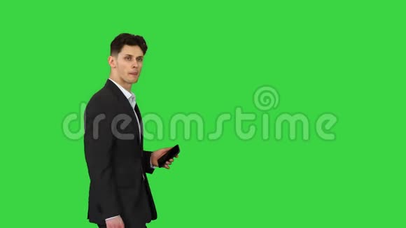 一位英俊的可疑商人手里拿着电话手里拿着公文包站在一个绿色的过来视频的预览图