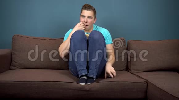 一个年轻人正在看电视和吃爆米花那家伙正在仔细看电视一个激动人心的时刻视频的预览图