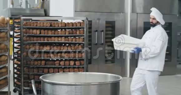 有胡子的年轻厨师面包师准备面团在一个大容器里再加一些面粉背景面包师工人带着视频的预览图