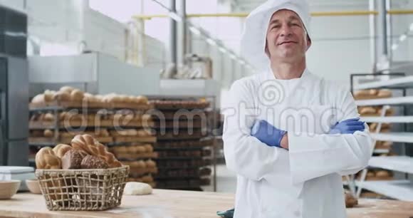 有魅力的老面包师穿着时尚制服直视镜头微笑着看着面包行业展示着巨大的视频的预览图