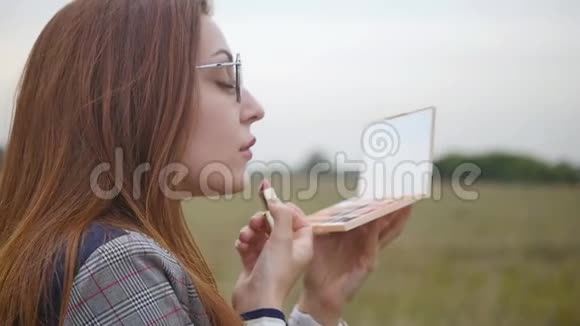 一个戴眼镜的年轻女子的肖像手里拿着一面镜子迷人的女人把她的嘴唇涂在背景上视频的预览图