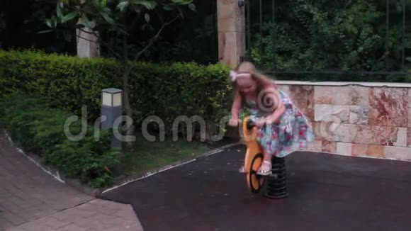 晚上一个穿着漂亮裙子的小女孩在操场上玩耍骑在摇摆玩具上视频的预览图