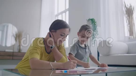妈妈和儿子坐在白色房间的镜子桌前用彩色铅笔画画笑着笑着视频的预览图
