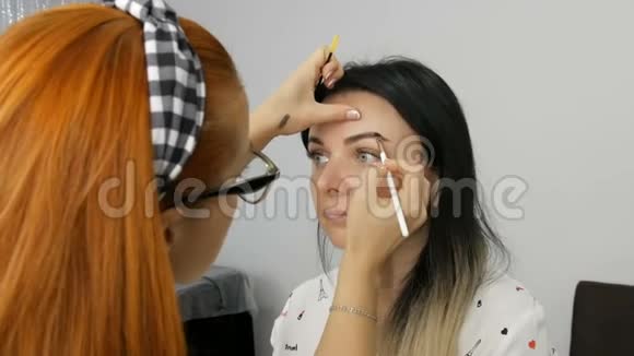 化妆师红色头发和眼镜谁做专业化妆美丽的晚妆应用于一个年轻人视频的预览图