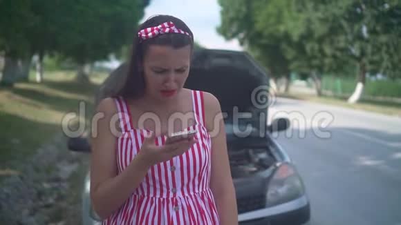 一名怀孕的年轻妇女站在一条乡村道路上的一辆失事汽车附近心烦意乱的女孩打电话寻求帮助视频的预览图