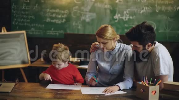 快乐的家庭年轻父母用铅笔画着色图帮助可爱的孩子男孩享受谈话游戏背景视频的预览图