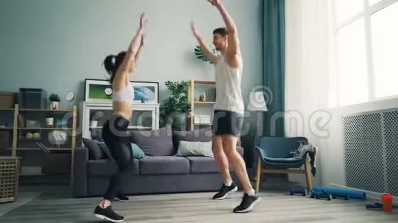 快乐的人在一起穿运动装做运动跳跃在家里举起手臂视频的预览图