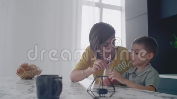 年轻的妈妈和儿子在厨房里用糖果喝果汁快乐的母亲和儿子慢慢地坐在桌子上视频的预览图
