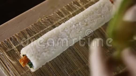 寿司大师的手在竹席上用鳄梨片装饰寿司卷寿司制作工艺把寿司卷滚起来视频的预览图