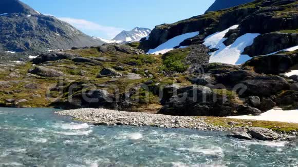 在一个阳光明媚的日子里挪威高山岩石地形上的积雪迅速融化的河流雪顶峰被看到视频的预览图