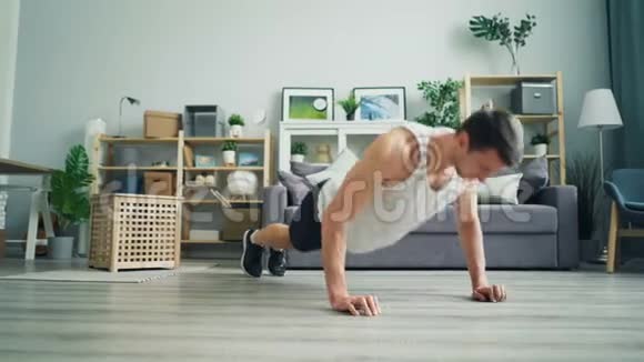 肌肉发达的黑发男人穿着舒适的衣服在家做俯卧撑视频的预览图