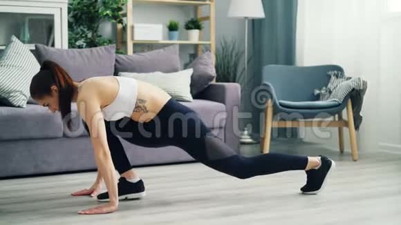 漂亮的年轻女子在家里运动服训练在地板上伸展腿视频的预览图
