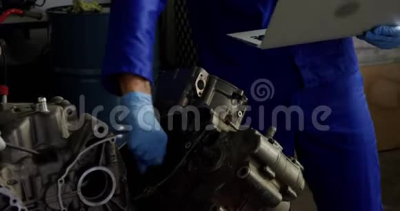 男机修工在修车厂修理摩托车发动机时使用笔记本电脑视频的预览图