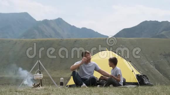 父子俩坐在帐篷附近篝火旁哈哈大笑视频的预览图