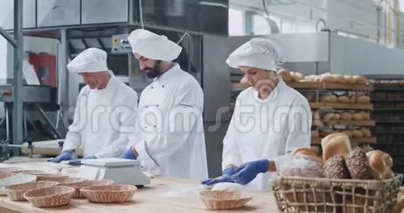 美丽的面包厂时尚的面包师两个男人和一个女人一起制作面团来烘焙面包视频的预览图