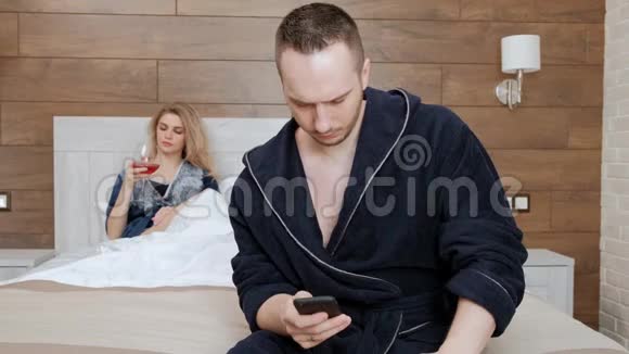 一对年轻的已婚夫妇穿着浴袍躺在酒店房间卧室的一张白色床上一个男人在视频的预览图
