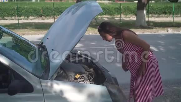 一名孕妇站在农村公路上的一辆失事汽车附近心烦意乱的女孩不知道如何处理崩溃视频的预览图