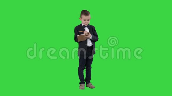 穿着正式衣服的男孩在绿色屏幕上的支票单或笔记本上写着Chroma键视频的预览图