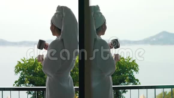 穿着浴袍的女孩喝咖啡俯瞰大海视频的预览图