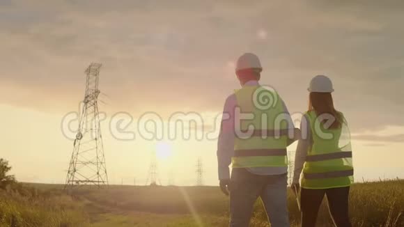 从后面看两名工程师一男一女戴着头盔拿着一块石碑的工程师在野外行走视频的预览图