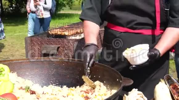 一个穿着黑色衣服和手套的厨师把香喷喷的皮拉夫放在一个盘子里放在一个巨大的大锅里的街头食物上街头节日视频的预览图