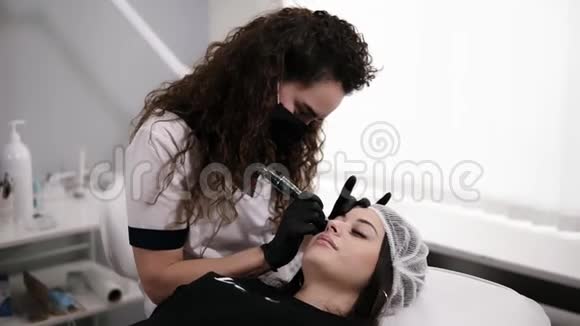 穿着卷发白色长袍的美容师正在为女性画眉或用针修正眉毛视频的预览图