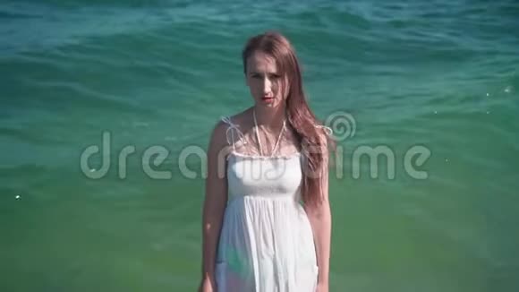 一个穿着白色海滩礼服的女孩站在海边一个光着脚的漂亮女孩站在海边视频的预览图