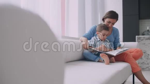 爱的母亲教她的儿子读拿书在家里的沙发上说话视频的预览图
