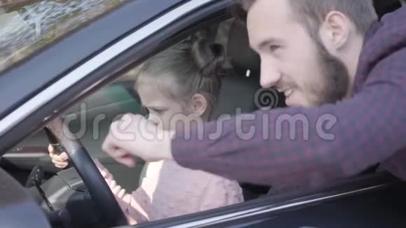 坐在驾驶座上的小女孩汽车靠近了站在女儿旁边的车旁的一个满脸胡须的男人视频的预览图